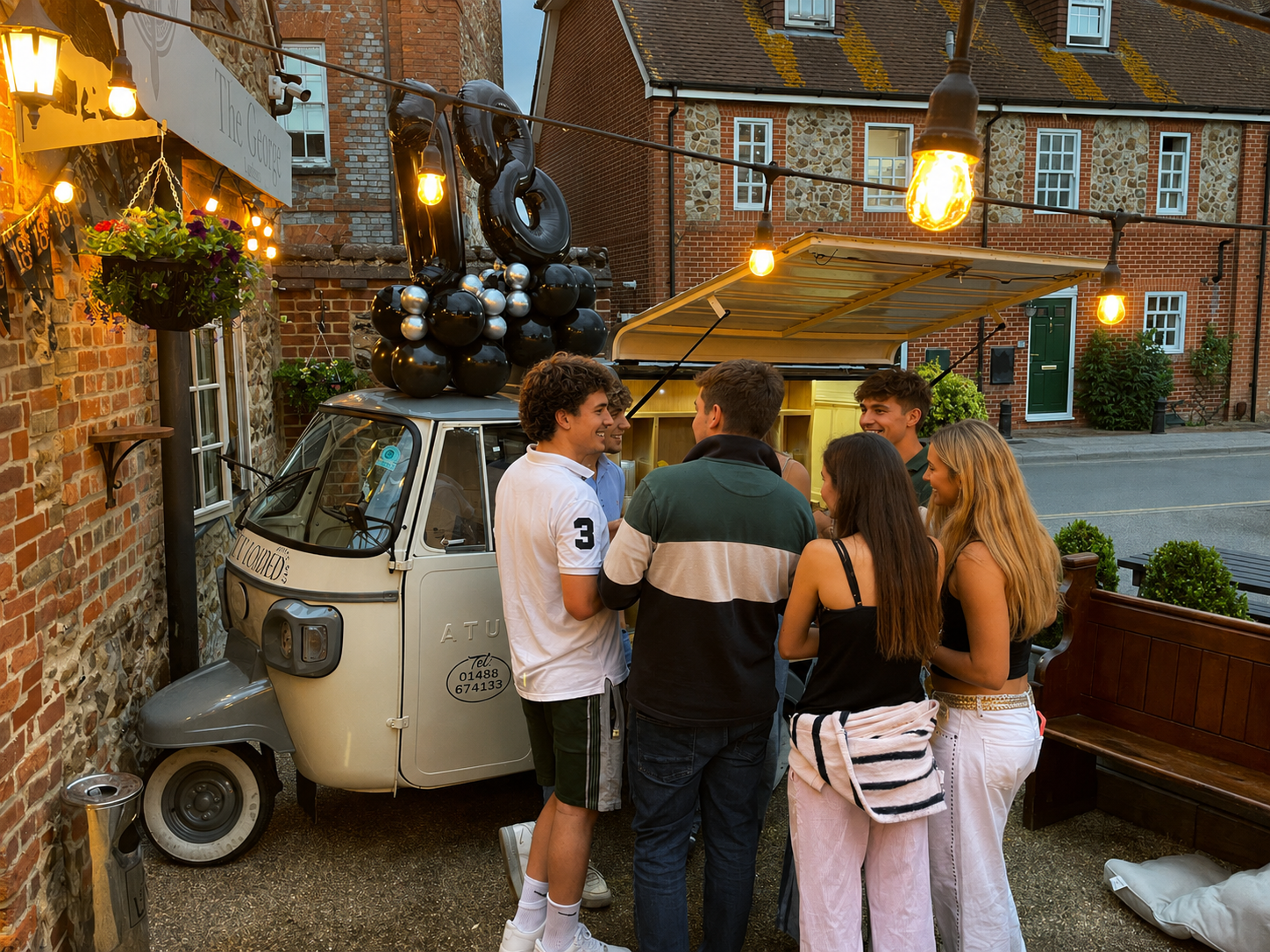 Guests gathered around the tuktuk bar at an evening party under festoon lights
